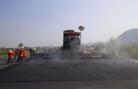 2019年8月，宜春經(jīng)開區(qū)S311路面攤鋪現(xiàn)場，工友們輔助路面兩側(cè)的分料、補窩等作業(yè)